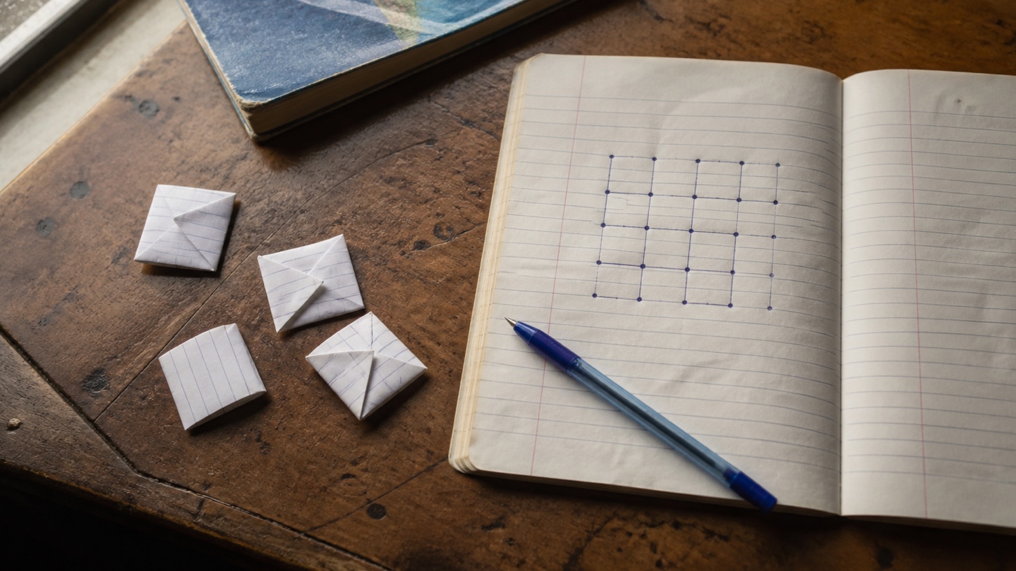 A school notebook surrounded by pens, folded chits and hand-drawn classroom games.